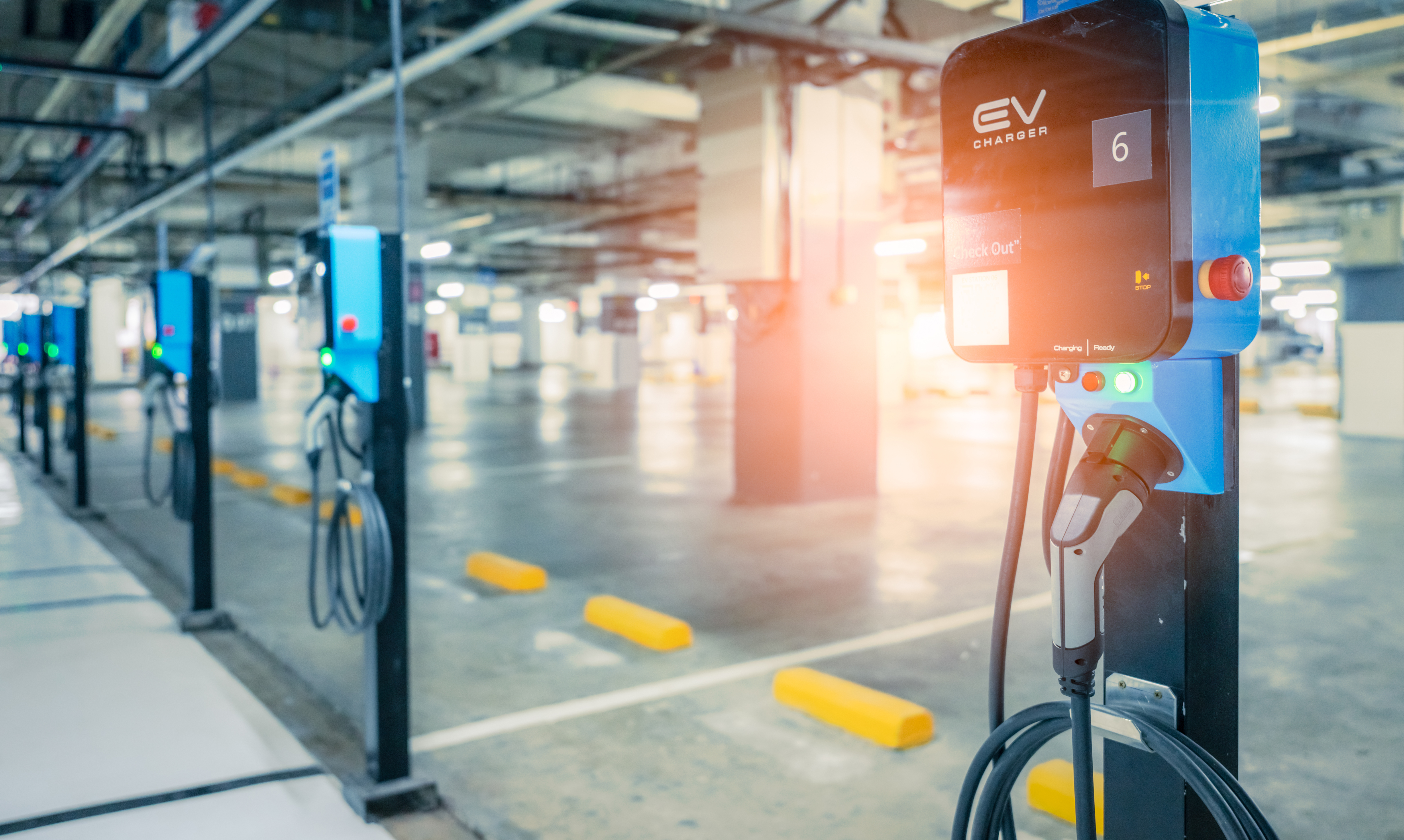 Blurred electric car charging station for charge EV battery. Plug for vehicle with electric engine. EV charger. Clean energy. Charging point at car parking lot. Future transport technology.