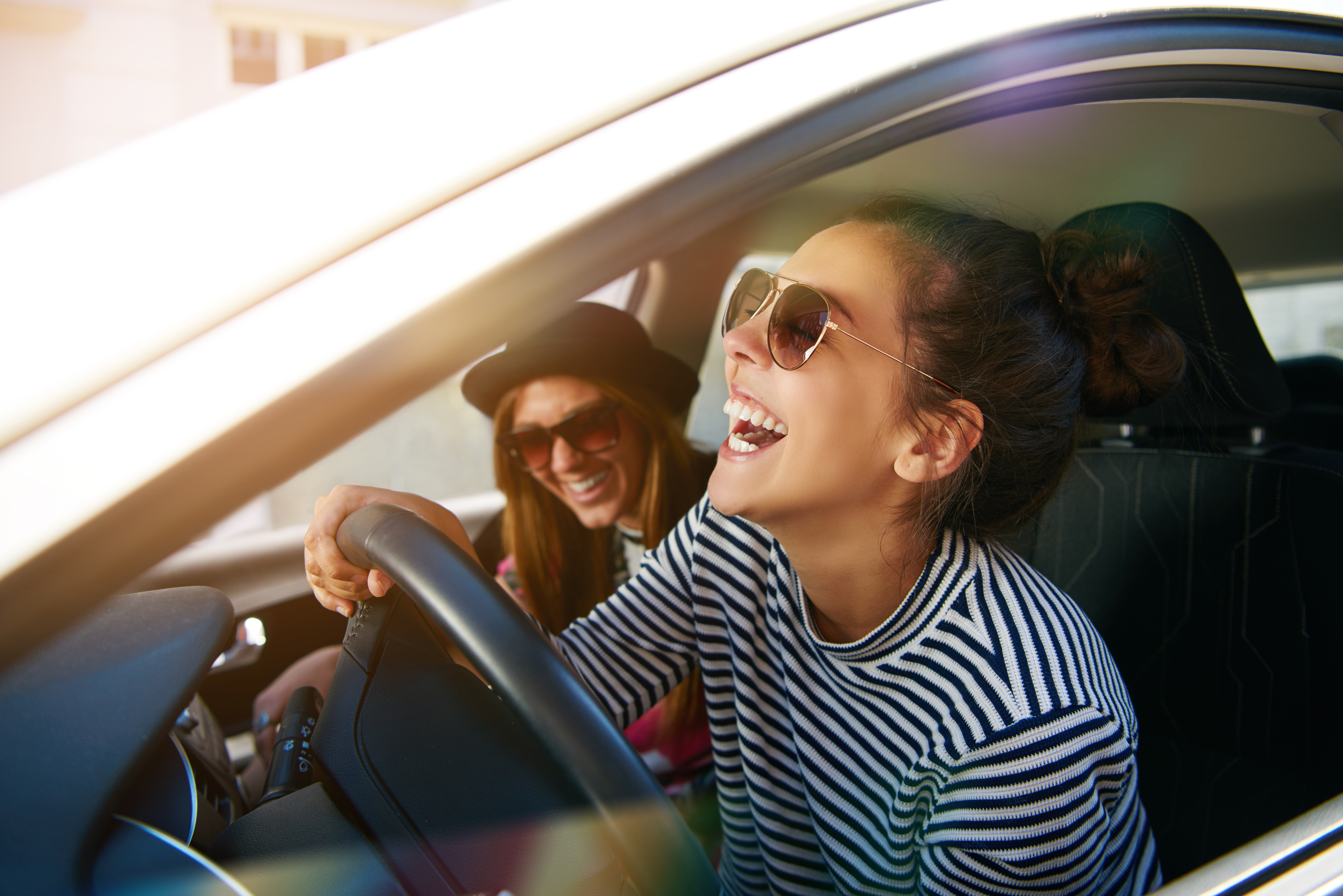 529724287 Laughing young woman wearing sunglasses driving a car with her girl friend , close up profile view through the open window; Shutterstock ID 529724287; purchase_order: ; job: 1287385; client: Hertz US; other: Cem Tezgoren