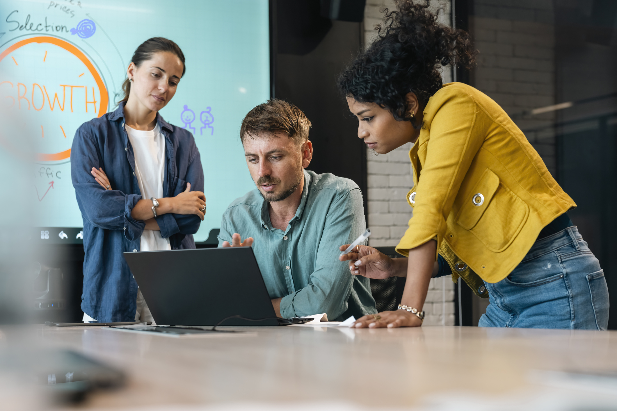 Small group of co-workers working together in a startup business office space. A team of young people in a modern office is discussing their project. Group of business people working. The team are sitting at a board room table looking at a laptop computer.